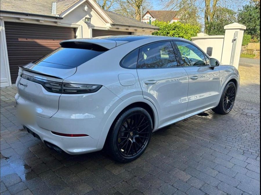 Pale grey Porsche Cayenne Coupe with black alloy wheels on a block-paved drive.