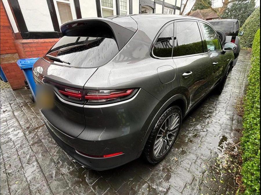 Grey Porsche Cayenne on a wet block-paved drive, with raindrops on the paint.