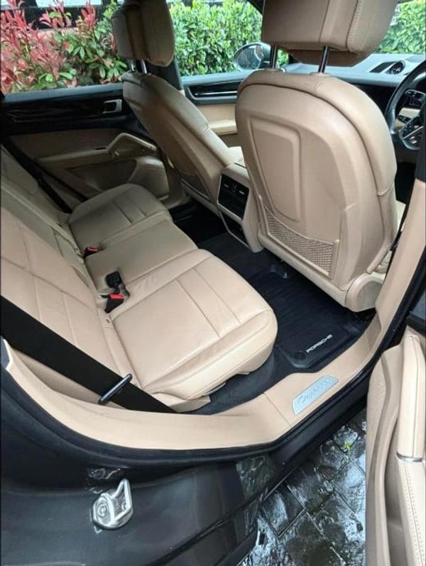 Tan leather rear seats and a black floor mat inside a Porsche, seen through the open rear door.