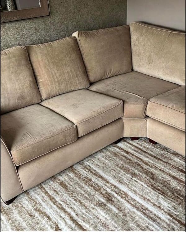 Beige velvet corner sofa on a striped cream rug in a living room.