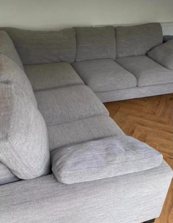 Light grey fabric corner sofa on a herringbone wood floor.