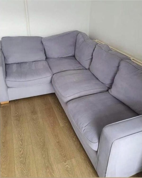 Lilac-grey corner sofa in a bare room with a wood-effect floor.